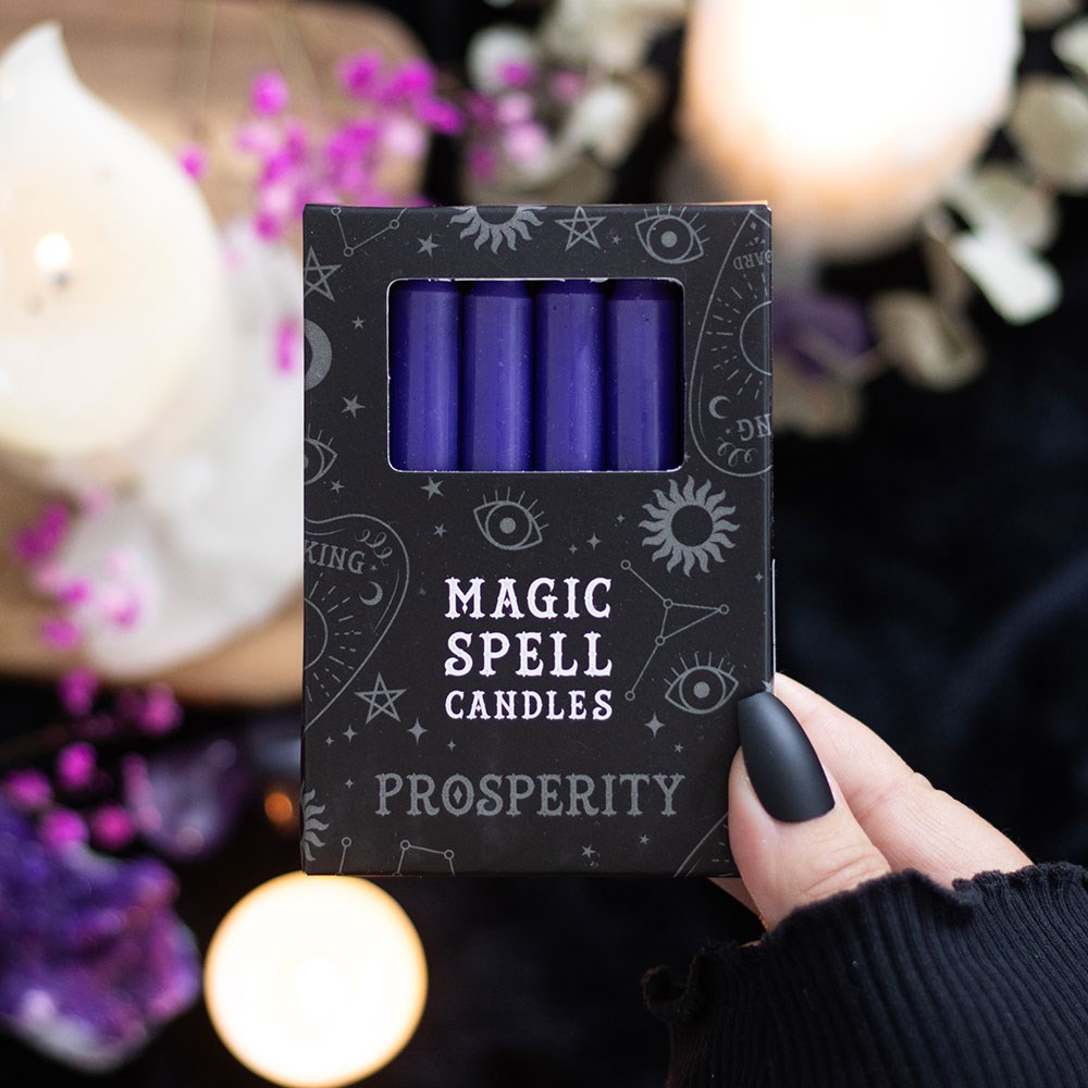 Pack of purple 'Magic Spell Candles Prosperity' held by a hand with a blurred candlelit background.