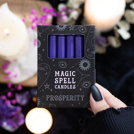 Pack of purple 'Magic Spell Candles Prosperity' held by a hand with a blurred candlelit background.