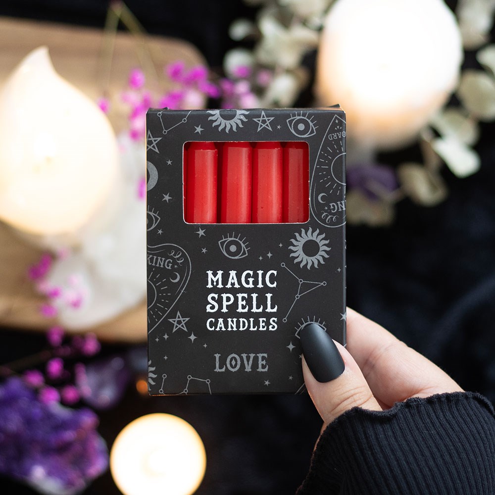 Pack of red candles labeled 'Magic Spell Candles Love' held by a hand with a blurred candlelit background.