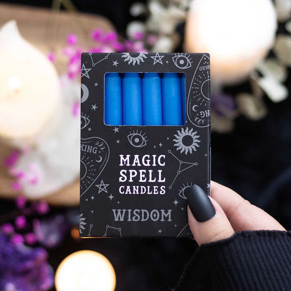 Pack of blue candles labeled 'Magic Spell Candles Wisdom' held by a hand with a blurred candlelit background.