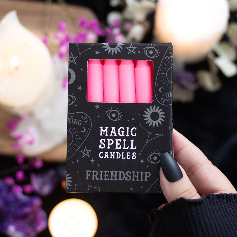 Box of pink 'Magic Spell Candles' for friendship held by a hand with a blurred candlelit background.