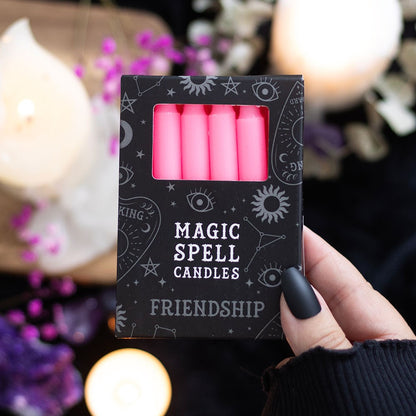 Box of pink 'Magic Spell Candles' for friendship held by a hand with a blurred candlelit background.